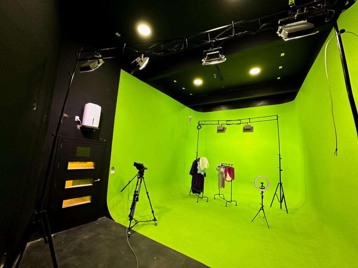 Estúdio C: ciclorama de chroma key verde inteiro, com câmera em tripé com rodinhas e arara de figurino