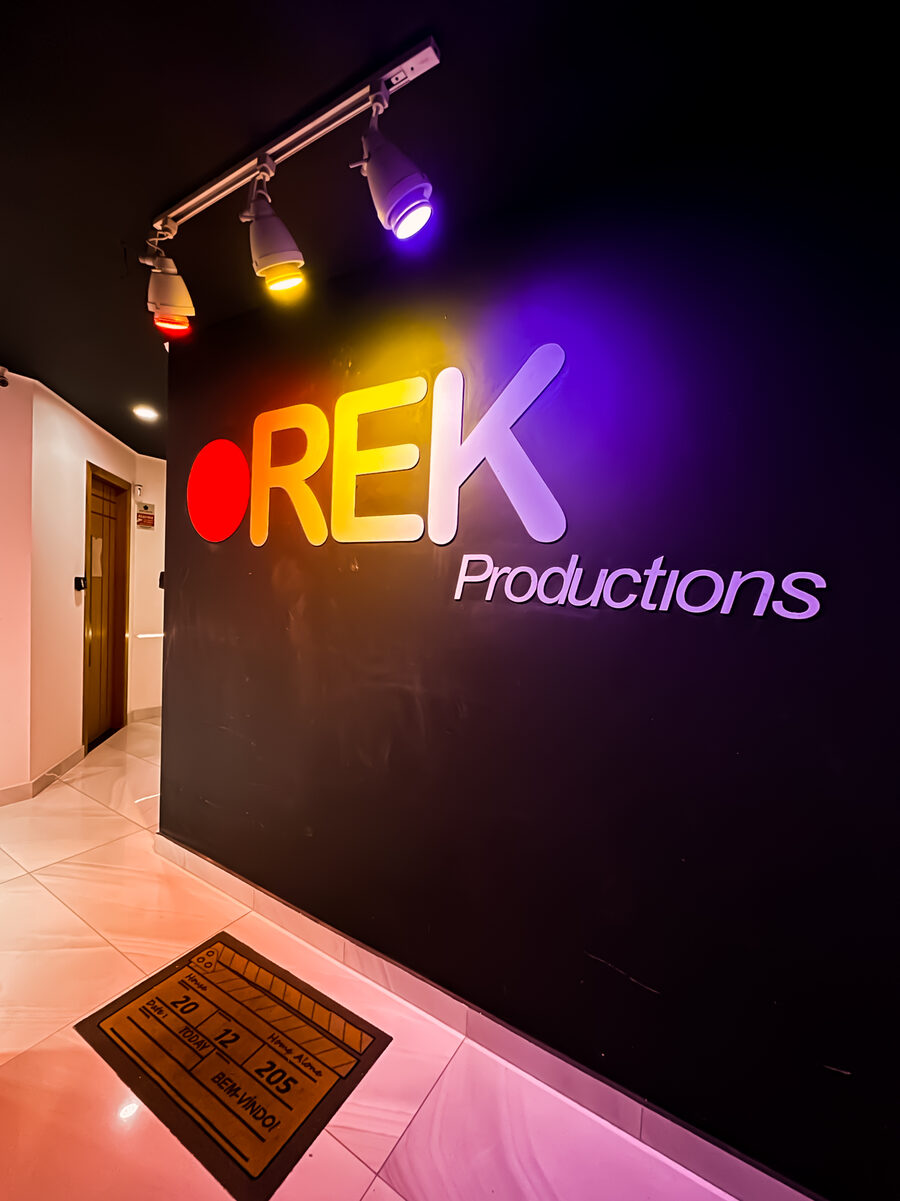 Corredor de entrada com a marca REK Productions iluminada na parede